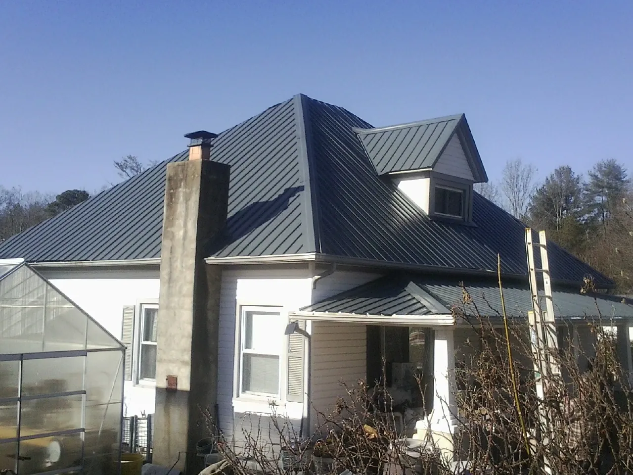 Dark blue standing seam metal roof on a white farmhouse with dormer — Slate & Tile Roof Repair by Roofing Brothers in O Brien