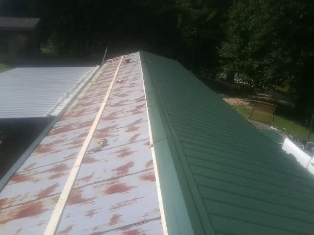 Old rusted panels beside newly installed green metal roofing — Wind Damage Roof Repair by Roofing Brothers in O Brien